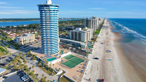 Un hotel frente al mar con una destacada torre cilíndrica y una cancha de tenis.