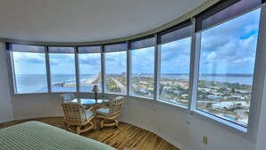 A room with a curved wall, large windows, a bed, a table, and two chairs. - SHORE BEATS WORK- Ocean/ River Views-, Pool HotTub, Game Rooms, WiFi PP19SW (Daytona Beach)