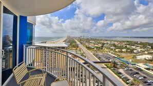 A balcony with a view of a beach, cityscape, and parking area. - SHORE BEATS WORK- Ocean/ River Views-, Pool HotTub, Game Rooms, WiFi PP19SW (Daytona Beach)
