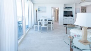 A spacious living area with a dining table, chairs, a glass coffee table, and a kitchen in the background. - SEA FOREVER 2/2 Great Ocean and River Views Pool & HotTub 20NW (Daytona Beach)