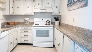 A kitchen with white cabinets, a stove, a coffee maker, and a painting on the wall. - SEA FOREVER 2/2 Great Ocean and River Views Pool & HotTub 20NW (Daytona Beach)