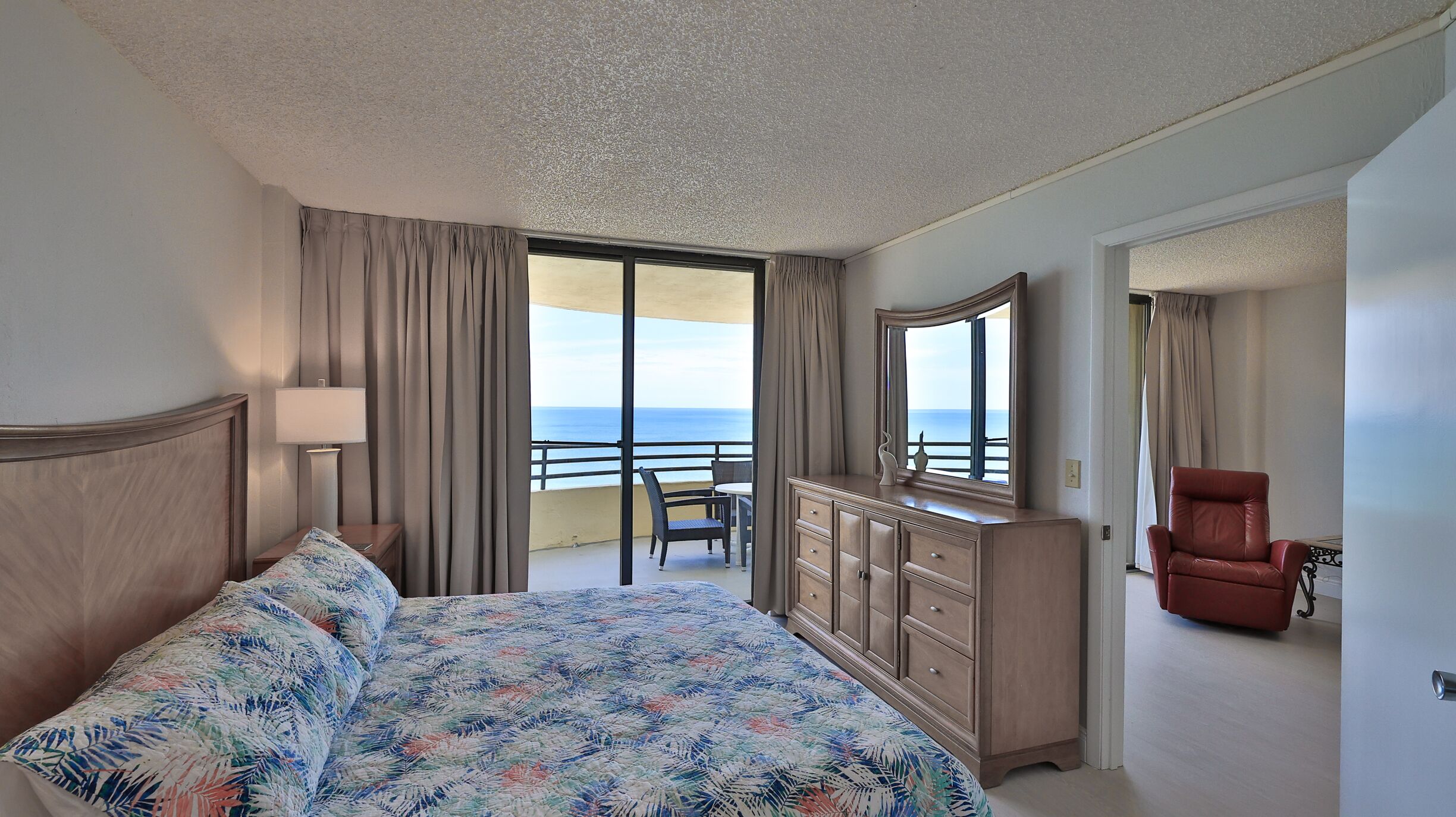 Een hotelkamer met een bed, een dressoir, een stoel en een balkon met uitzicht op de oceaan.