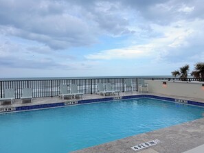 A pool with a 4 ft. 9 in. depth, adjacent to a beach with chairs and a railing.