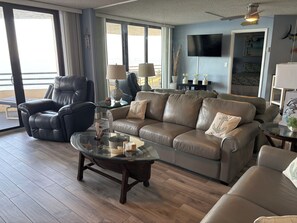 A living room with a leather sofa, a glass coffee table, and a television mounted on the wall.