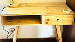 Un escritorio de madera con una lámpara, un cajón y una pequeña estantería.