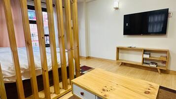 Een kamer met een bed, een houten bureau, een televisie en een raam met uitzicht op gebouwen.