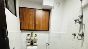 Un baño con inodoro, ducha y bañera. Hay un armario de madera sobre el inodoro y una pequeña estantería con plantas en macetas.