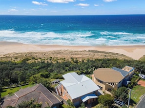 Une propriété située sur la côte, avec vue sur la plage, comprenant une grande maison dotée d’un toit incurvé et un bâtiment plus petit avec un toit plat.