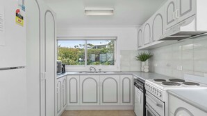 A modern kitchen with white cabinetry, a built-in oven, a stovetop, and a window with a view of greenery outside.