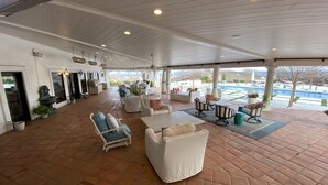 A spacious covered patio area with multiple seating options, including sofas and chairs, and a view of a swimming pool and landscape.