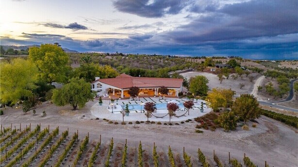 A vineyard with rows of grapevines, a large building with a red roof, and a pool area.