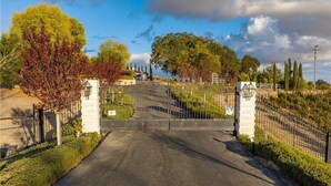 A gated driveway leading to a building with a stone facade, surrounded by trees and a clear sky.
