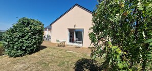 A house with a wooden deck, a glass door, and a small table with chairs. - Gîte du Puech 2-3 personnes (RIEUTORT DE RANDON)