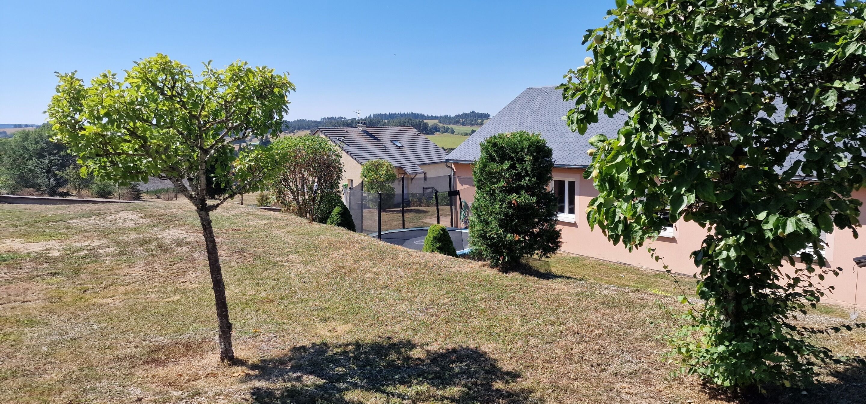 Un quartier résidentiel avec une maison, une cour clôturée et un ciel dégagé.