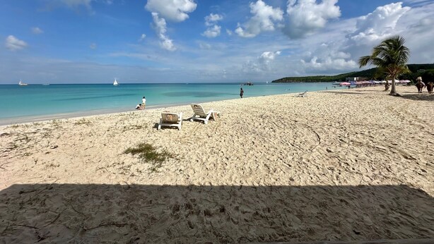 Ein Strand mit blauem Himmel, sandigem Ufer und ein paar Booten in der Ferne.