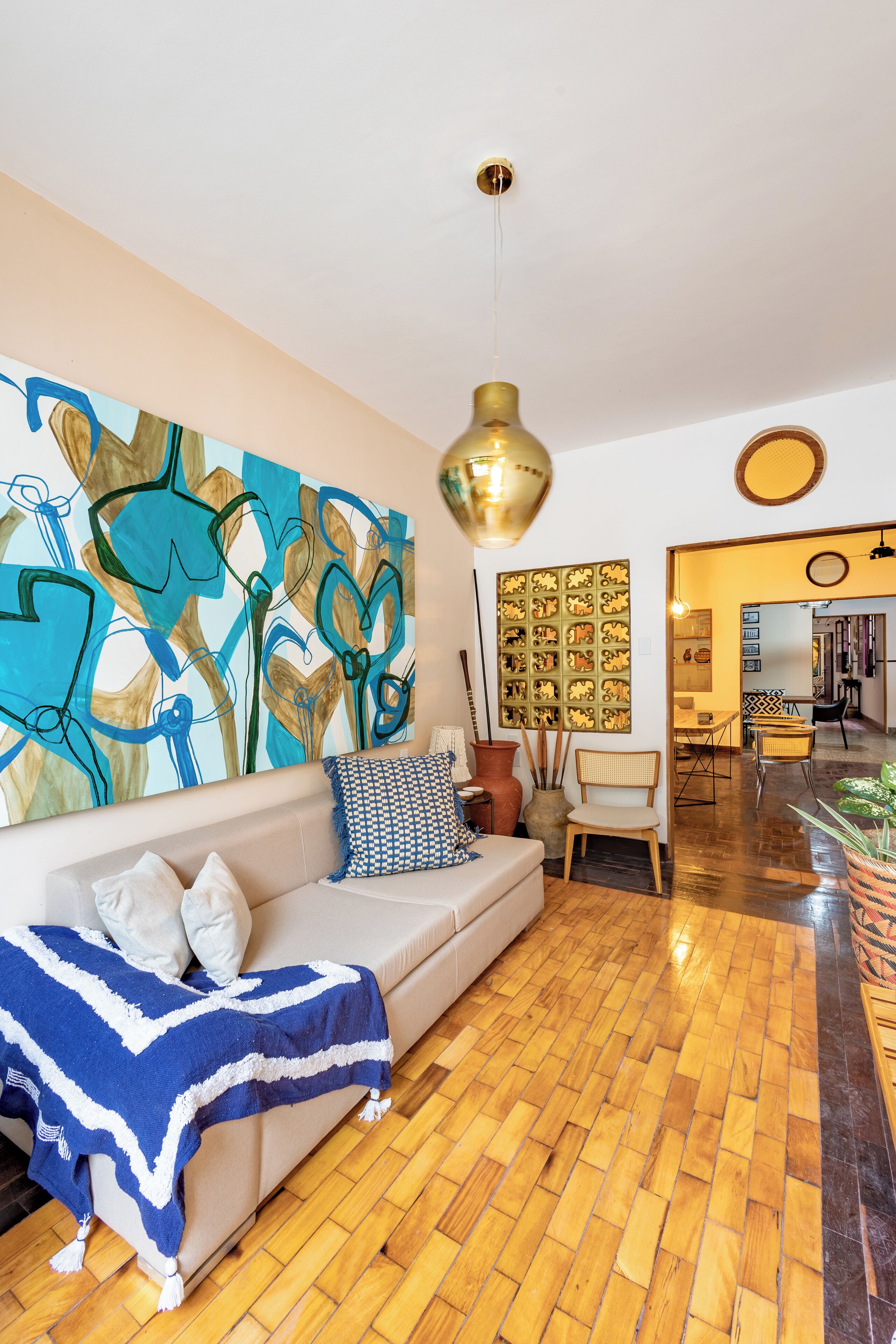 Una sala de estar con un sofá, un cuadro abstracto grande, una lámpara colgante y una zona de comedor al fondo.