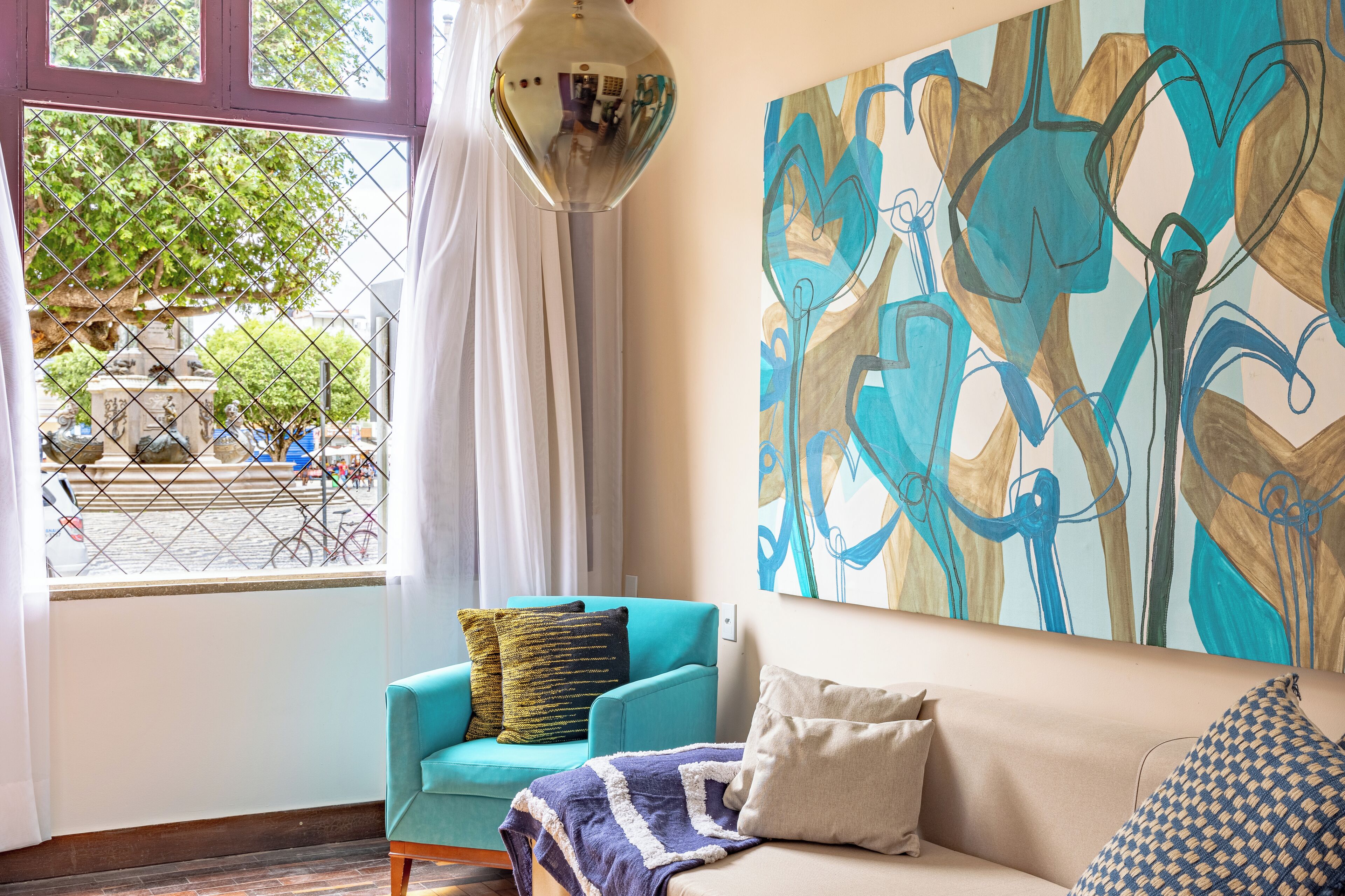 Ein Zimmer mit einem türkisfarbenen Sessel, einem beigen Sofa und einem großen, abstrakten Gemälde an der Wand.