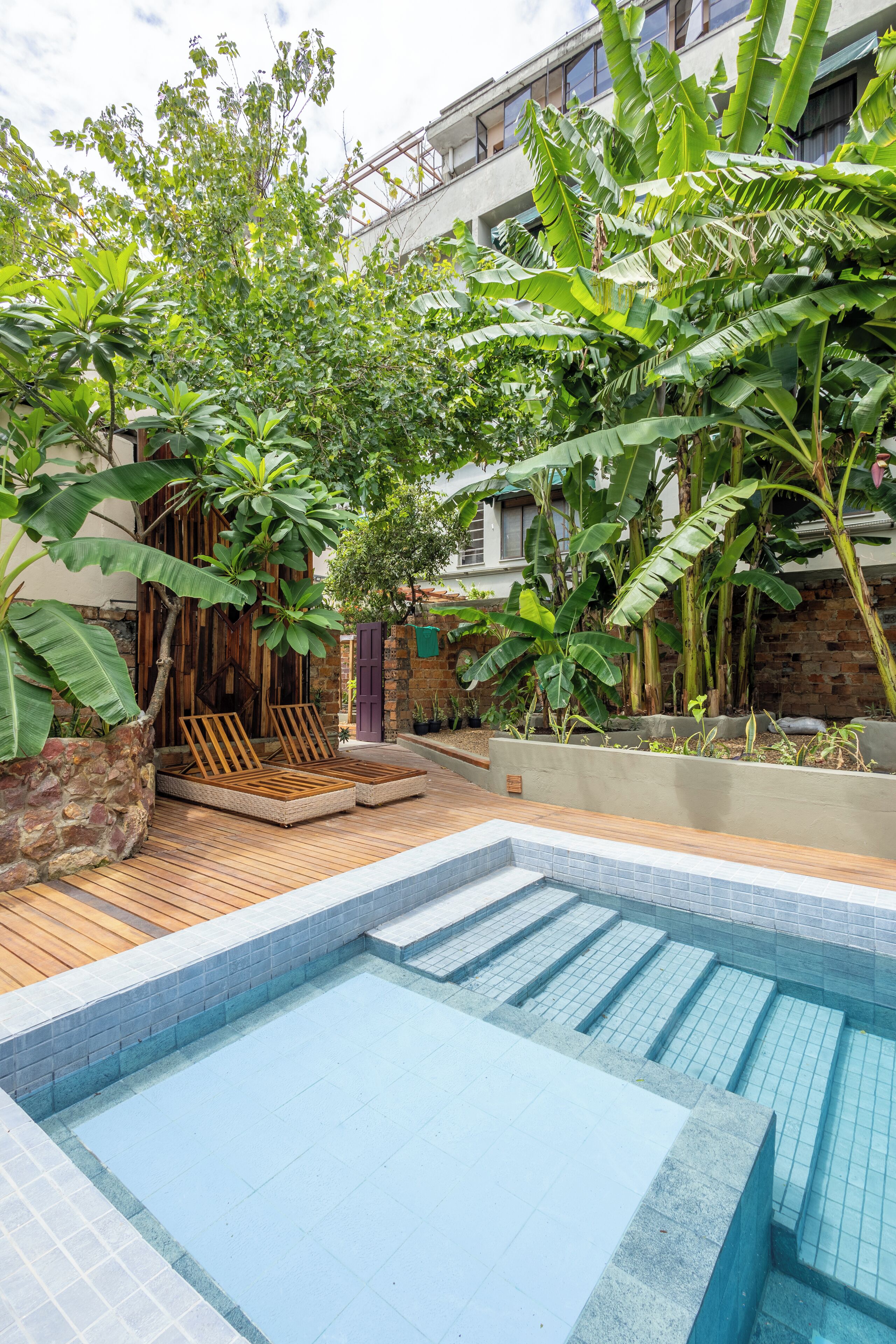 A swimming pool with wooden deck seating and lush greenery.