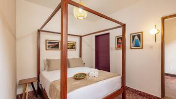 A four-poster bed with a wooden frame, a white bedspread, and a beige throw blanket. There is a small wooden nightstand to the left of the bed.