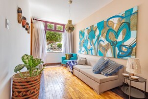 Una sala de estar moderna con un sofá beige, un cuadro abstracto grande, una planta en maceta y piso de madera.