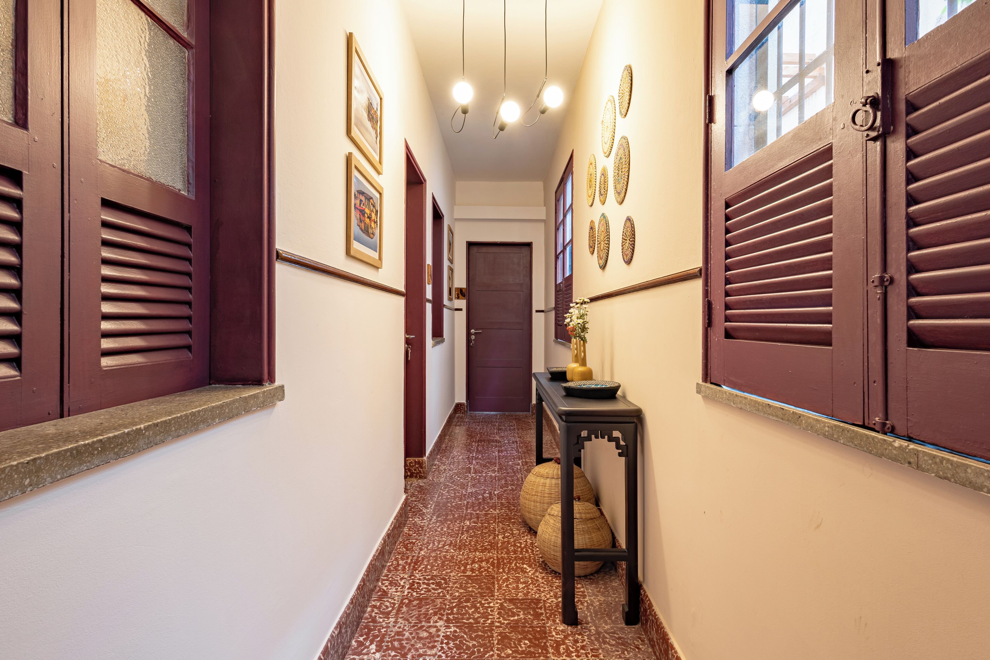 Um corredor com piso estampado, uma porta no final e uma pequena mesa com objetos decorativos.