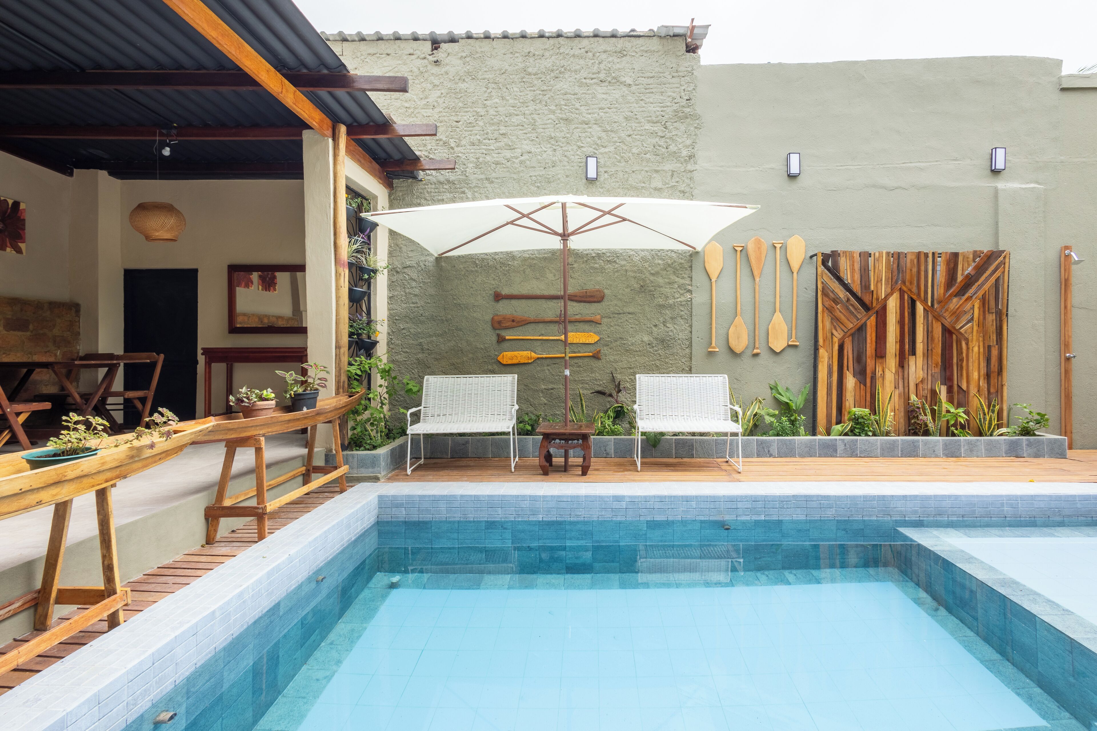 Zona de piscina con dos sillones blancos, una mesa de madera y una sombrilla.