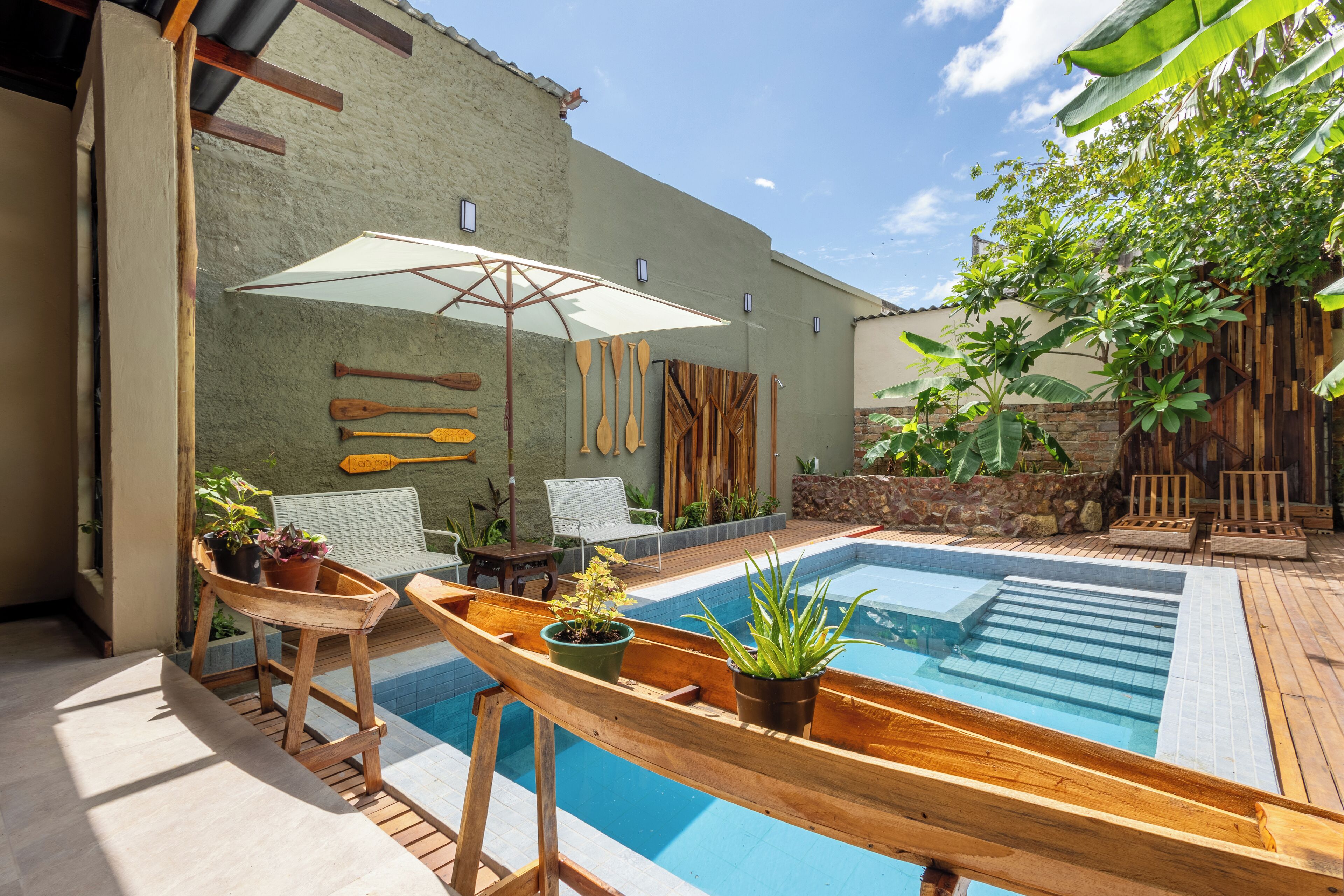 A backyard with a swimming pool, wooden deck, outdoor furniture, and potted plants.