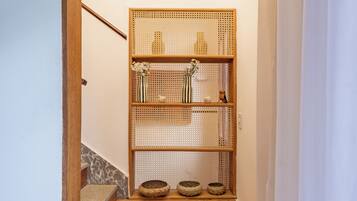 A wooden staircase leading to a landing with a ceiling fan, a woven shelf with decorative items, and a small wooden shelf above.