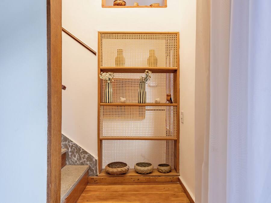 A wooden staircase leading to a landing with a ceiling fan, a woven shelf with decorative items, and a small wooden shelf above.