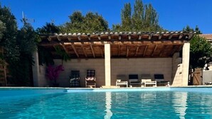 Una piscina azul cristalina con una pérgola de madera y sillones de descanso al fondo.