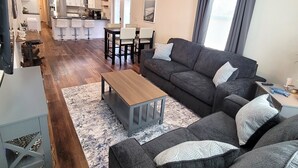 Un soggiorno moderno con un divano grigio, un tavolino in legno e una zona pranzo con cucina sullo sfondo.