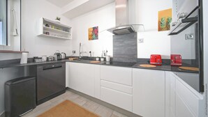 Una cocina moderna con armarios blancos, encimera negra, lavavajillas, estufa y dos electrodomésticos rojos.