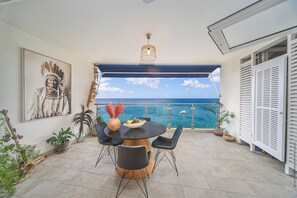 A balcony with a round table, chairs, and a view of the ocean. - Appartement Moana Martinique (Schœlcher)