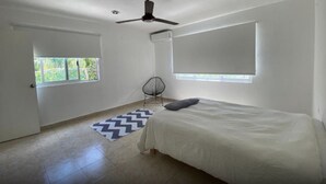A bedroom with a bed, a ceiling fan, a window, and a chair. - The Hostal Inn (Playa del Carmen)