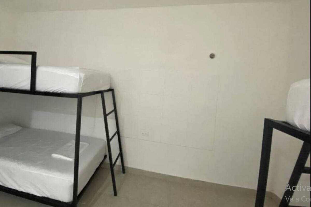 Uma cama beliche com escada, uma mesa pequena e uma parede branca lisa.