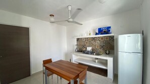 A compact kitchen with a wooden dining table, white cabinets, a white refrigerator, and a ceiling fan. - The Hostal Inn (Playa del Carmen)