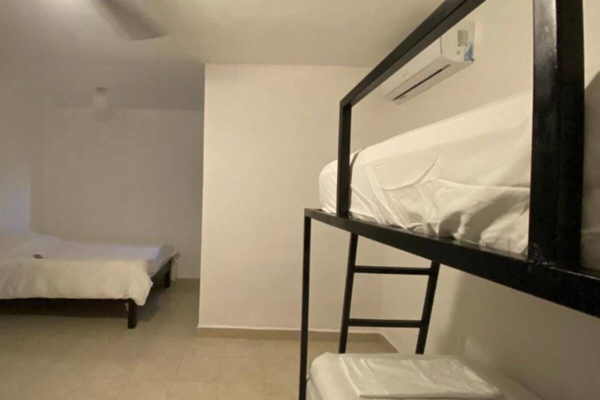 Quarto pequeno e simples com cama beliche e uma cama de solteiro. As paredes são lisas e o chão, de azulejo.