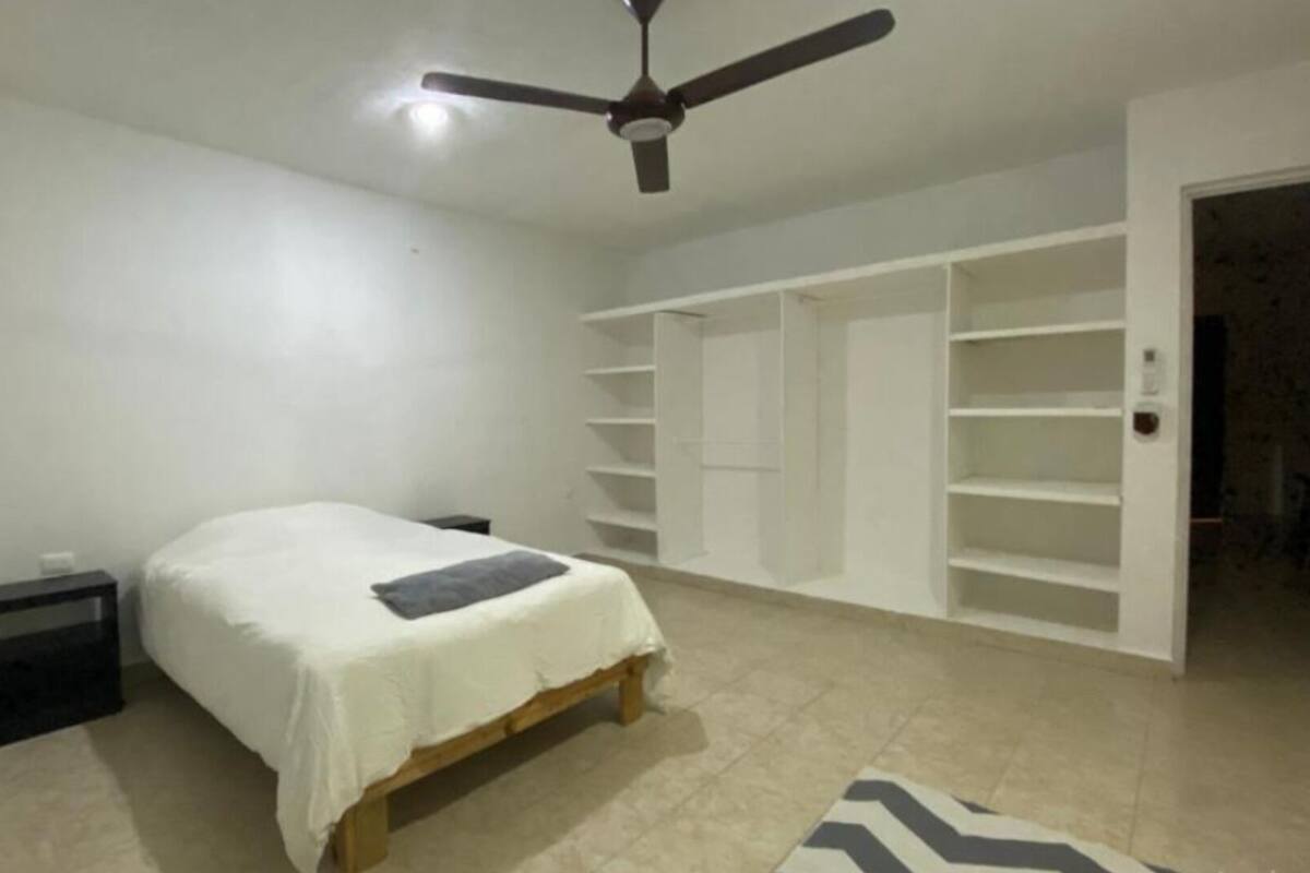 Quarto com cama, ventoinha no teto e estantes embutidas.
