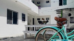 A turquoise bicycle parked in front of a white building with a bench and a hanging plant. - The Hostal Inn (Playa del Carmen)