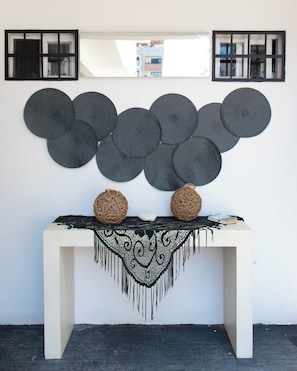 Um console branco com um jogo americano de franjas pretas e duas cestas trançadas. Acima da mesa, há três espelhos de parede com moldura preta e um grande painel circular pendurado na parede.
