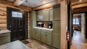 A log cabin interior with a kitchen area featuring green cabinets, a coffee bar, and a fire extinguisher. - The Birchwood Cabin - Stunning Mountain Views (Sunderland)