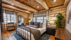 A log cabin bedroom with a bed, nightstand, and a large window. - The Birchwood Cabin - Stunning Mountain Views (Sunderland)