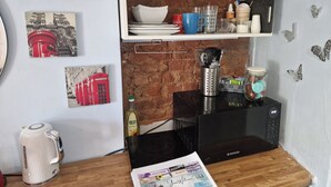 A kitchen with a microwave, kettle, and various kitchen utensils on shelves. There are framed pictures on the wall and a welcome pack on the counter.