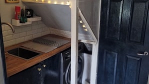 A compact kitchen with a sink, wooden countertop, and a washing machine. There are string lights and a sign for hot dogs.