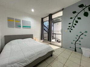 A bedroom with a bed, a window, a door, and a wall with a tree mural. - SJO Oasis Hostel (San José)