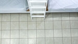 A room with a tiled wall, a white bed frame, and a ladder. - SJO Oasis Hostel (San José)