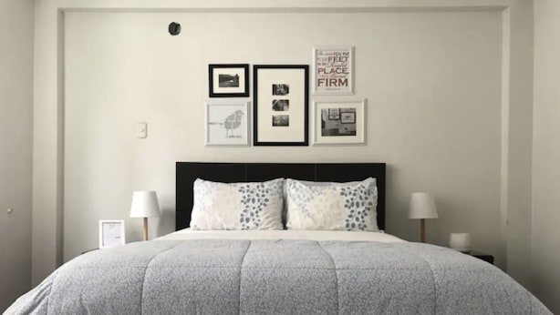 A neatly made bed with a grey quilt, two bedside lamps, and three framed pictures on the wall. - InkaHuset Airport (Callao)