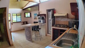 Een compacte keuken met een centraal kookeiland, barstoelen, een magnetron, een kookplaat en een spoelbak.