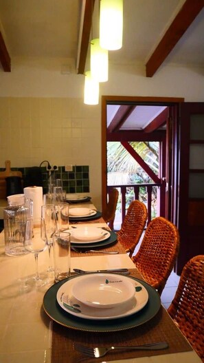 Une table à manger dressée avec des assiettes, des verres et des couverts, entourée de chaises en osier et offrant une vue sur la verdure environnante.