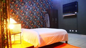 Une chambre à coucher comprenant un lit, un téléviseur fixé au mur, une armoire et un papier peint à motifs.